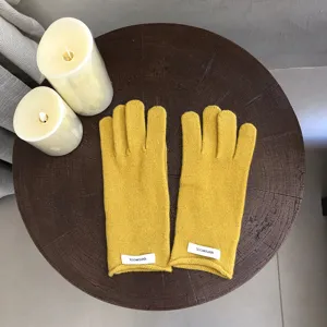 Close-up detail of yellow knit wool winter gloves on dark wooden table with candles.