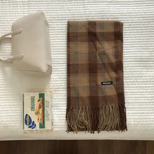 Klassisches braunes Karoschal-Detail mit Fransenrand und gewebtem Markenetikett.
