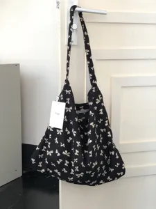 Black canvas shoulder bag featuring a cute white bow pattern, perfect for casual use.