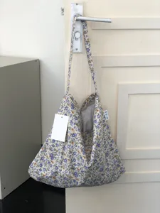 Detailaufnahme der geblümten Canvas-Umhängetasche mit großem Fassungsvermögen und Label.