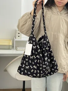 Detail shot of a black canvas tote bag featuring cute white bow prints and shoulder strap.
