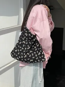 Detail shot of a black canvas shoulder bag featuring an all-over beige bow print design.