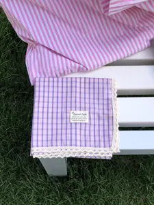 Detailaufnahme des violetten Karomustertuchs aus Baumwolle mit feiner weißer Spitzenborte.