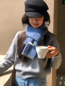 Nahaufnahme des kuscheligen blau-grau gestreiften Strickschals mit Markenetikett.