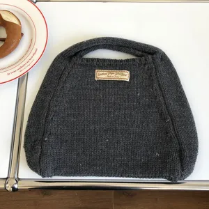 Nahaufnahme der dunkelgrauen Strickhandtasche auf weißem Tisch mit feiner Wolltextur.