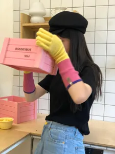 Close-up detail of color-blocked knit extended gloves worn in lifestyle kitchen scene.