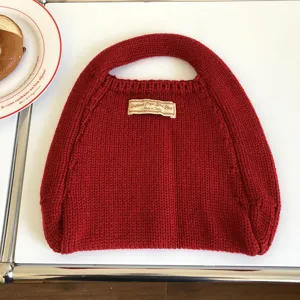Detailansicht einer roten Strickhandtasche mit strukturiertem Wollstrick und gewebtem Etikett.