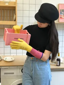 Detailed view of long color-block knitted gloves worn by model in a cozy kitchen setting.