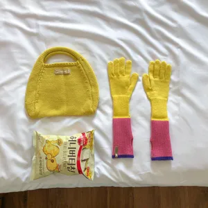 Detailed view of yellow knit handbag and color-blocked arm warmer gloves on white bedding.