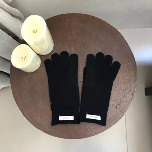 Detailed flatlay of black wool gloves on wooden table with warm candle decor for winter.