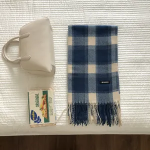 Blau-cremefarbener Karo-Winterschal mit Fransen und schwarzem Label, gemuetliches Detail.