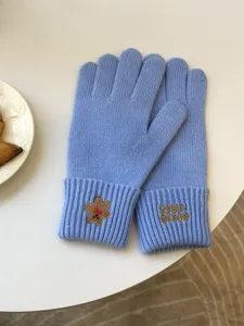 Detailed shot of light blue knit five-finger touchscreen gloves with cute bear and text embroidery.