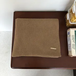 Detailansicht des eleganten braunen Strickschals aus Wolle mit Metallmarkenetikett.