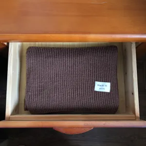 Detailansicht eines dicken braunen Strickschals fuer den Winter ordentlich gefaltet in Holzschublade