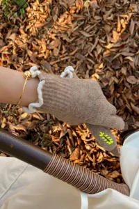 Detail shot of brown knit wool gloves featuring white ruffled cuffs and delicate finger embroidery.