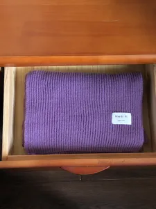 Nahaufnahme eines weichen, lila gestrickten Winterschals ordentlich in Holzschublade.