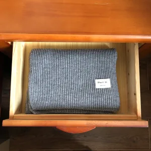 Detailansicht eines gemütlichen grauen Strickschals ordentlich in Holzschublade gefaltet.