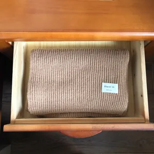 Detailaufnahme eines dicken Strick-Winterschals ordentlich in einer Holzschublade, braune Wolle.