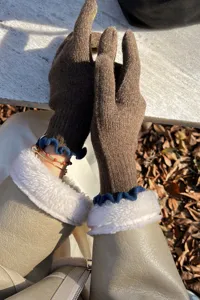Close-up of autumn winter brown knit gloves with blue ruffles and fluffy white cuffs.