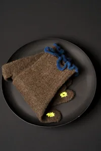 Close-up detail of brown knitted wool gloves with blue ruffle trim and yellow floral embroidery.