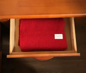 Detailansicht eines roten Strickschals, ordentlich in einer Holzschublade verstaut für Winter.