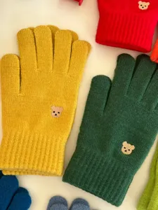 Dettaglio in primo piano di guanti in maglia a cinque dita con simpatico ricamo di orsetto.