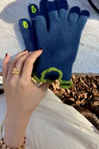 Close-up of blue knit touchscreen gloves with green ruffled cuffs and cute yellow embroidery.