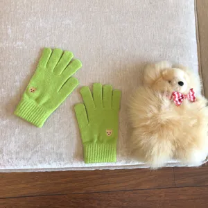 Primo piano di simpatici guanti in maglia verde con ricamo di orsetto e peluche.