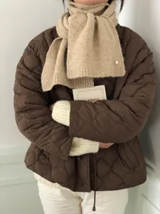 Nahaufnahme eines gemütlichen beigen Strickschals, kombiniert mit einer gesteppten Jacke.