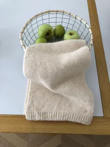 Nahaufnahme eines weichen beigen Strickschals im Korb mit grünen Äpfeln für den Winter.