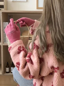 Detail shot of cozy pink knit gloves featuring a sparkling rhinestone bow, lifestyle winter wear.