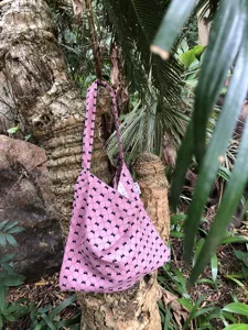 Detail shot of a pink canvas shoulder bag with black bow print, hanging on a tree in jungle.