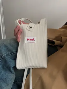 Primer plano de un mini bolso bandolera minimalista de punto acanalado en beige con etiqueta roja.