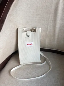 Detalle de mini bolso bandolera de punto, cartera beige con botón de presión y etiqueta frontal.