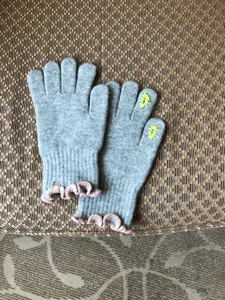 Grey knit gloves detail showing pink ruffle cuffs and cute finger embroidery, soft winter.