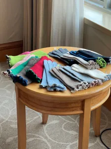 Close-up of colorful knitted touchscreen gloves with ruffled cuffs laid on a wooden table.
