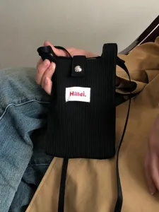 Detalle en primer plano de un elegante bolso bandolera de punto negro para teléfono.