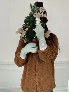 Gros plan de gants en tricot vert clair douillets tenus avec un sapin de Noël, accessoire d'hiver