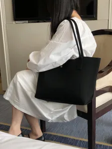 Gros plan d'un sac cabas tricoté noir minimaliste porté sur l'épaule dans un intérieur cosy.