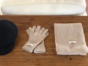 Detailed view of cozy knit wool scarf, matching gloves, and hat on wooden table. Soft texture.