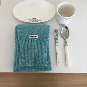Detailaufnahme eines gemütlichen blau-grünen Strickschals mit Etikett im minimalistischen Stil.