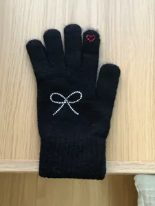 Close-up of black knit winter glove featuring sparkling rhinestone bow detail and red heart.