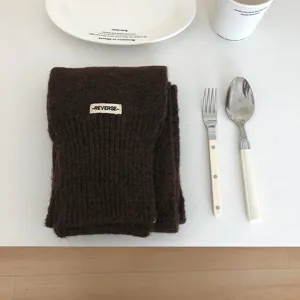 Detailansicht eines kuscheligen dunkelbraunen Strickschals mit gewebtem Etikett, flachgelegt.