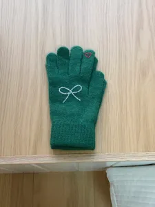 Close-up of green knitted winter gloves featuring sparkling rhinestone bow and heart detail.