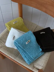 Nahaufnahme von vier bunten gefalteten Strickschals mit gewebten Etiketten auf Stuhl.