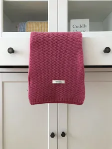Close-up detail of soft pink knit wool scarf hanging on cabinet showcasing texture.