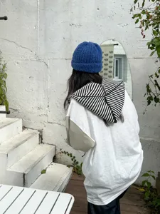 Outdoor detail view of a warm blue knit beanie and black white striped hooded scarf combo.