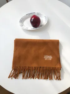 Detailansicht eines gemütlichen karamellfarbenen Wollschals mit Stickerei und Fransen.
