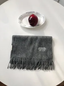 Nahaufnahme des einfarbigen grauen Wollschals mit feinen Fransen und dezenter Stickerei.