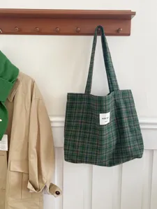 Detailed view of green plaid wool tote bag hanging in cozy lifestyle scene with autumn coat.